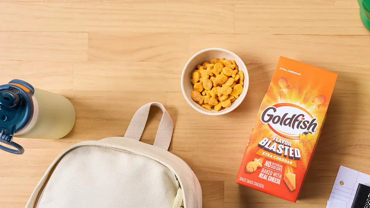 Goldfish Flavor Blasted Xtra Cheddar crackers with school supplies, a backpack, and a bowl of crackers.