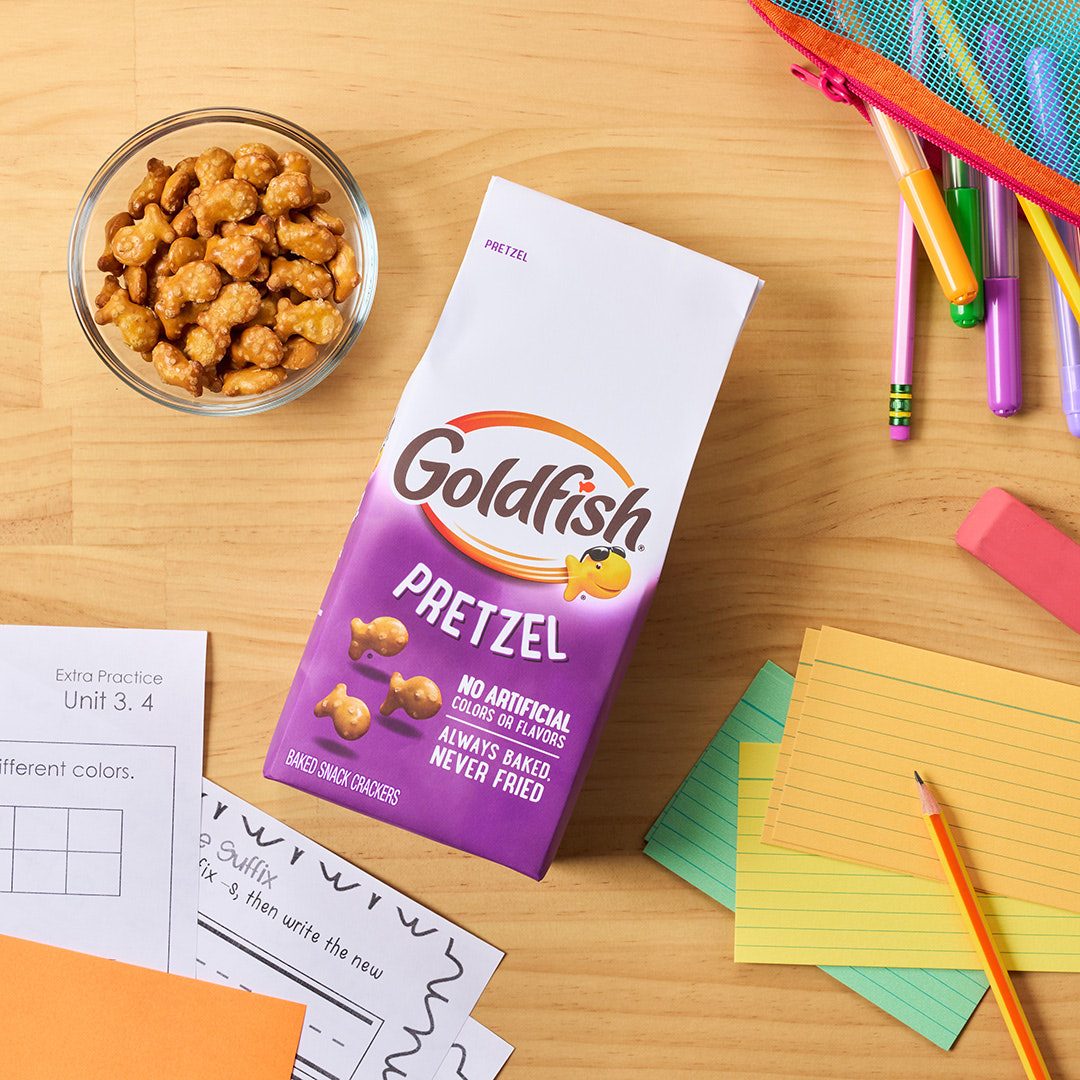 Goldfish Pretzel crackers with a bowl of pretzel crackers, school supplies, and homework materials on a wooden table.