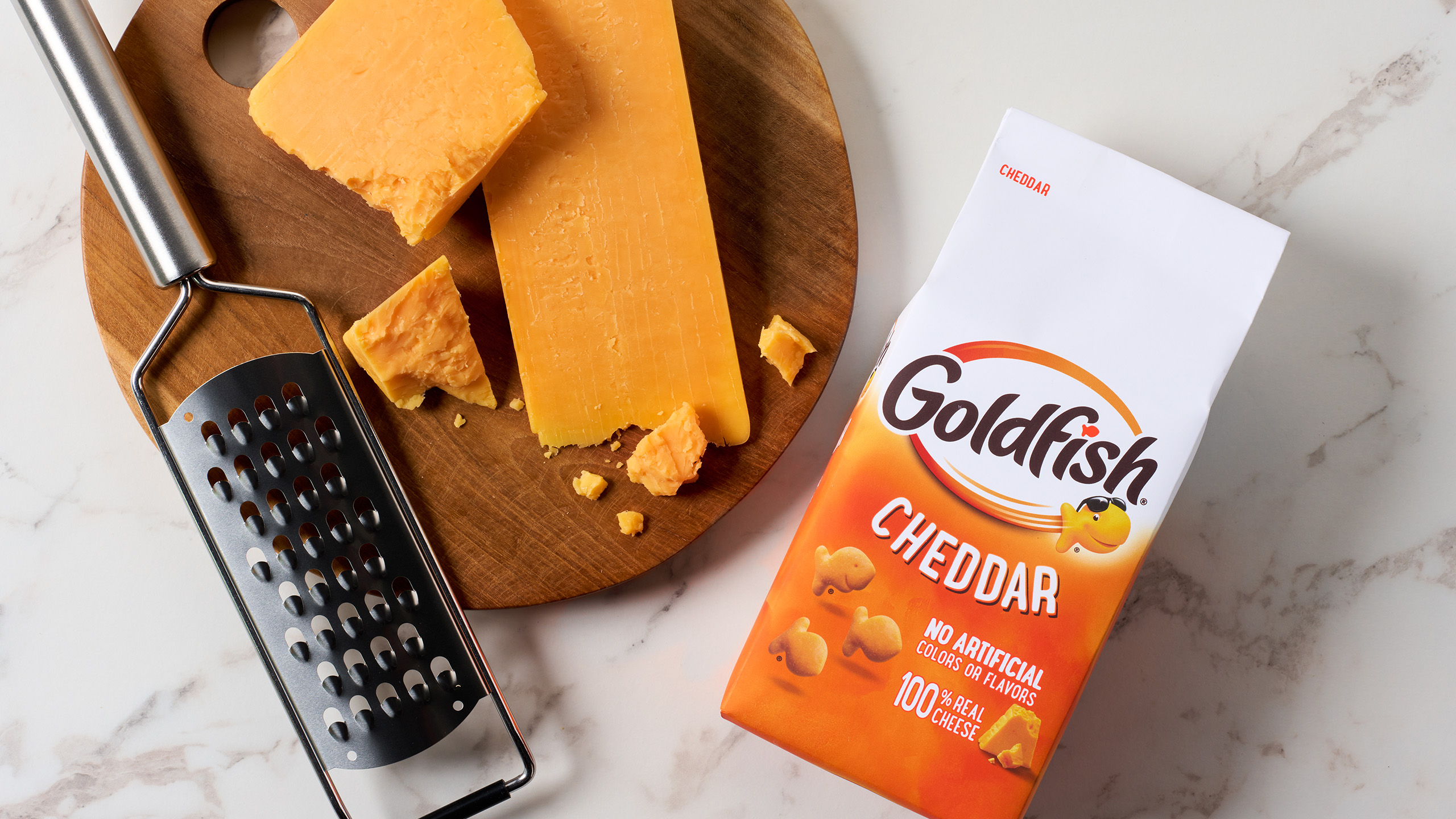 Goldfish Cheddar crackers beside a wedge of cheddar cheese on a serving board.