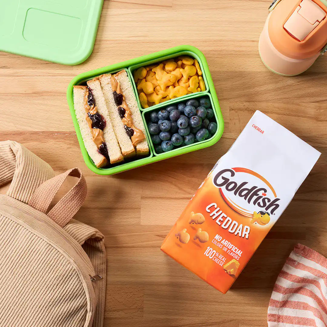 Packed lunch with a peanut butter and jelly sandwich, fruit, and Goldfish Cheddar crackers.