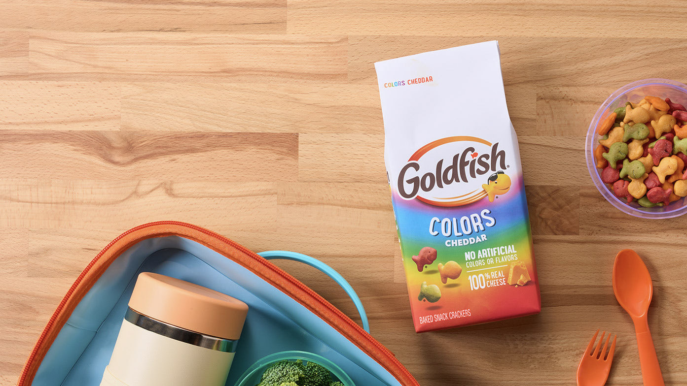 Goldfish Colors Cheddar crackers paired with grapes, broccoli, reusable lunch containers, and utensils for a packed lunch.