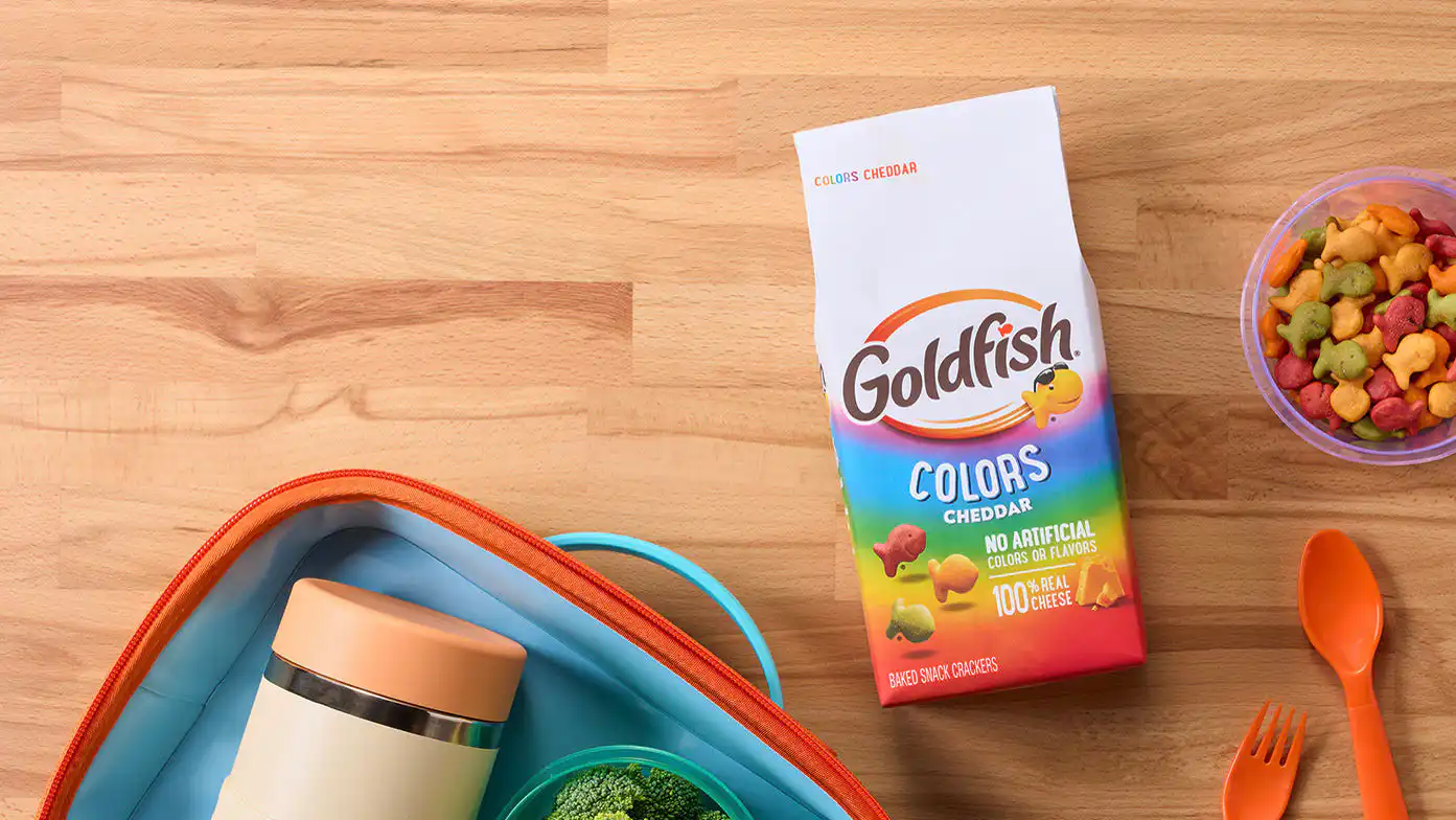 Goldfish Colors Cheddar crackers paired with grapes, broccoli, reusable lunch containers, and utensils for a packed lunch.