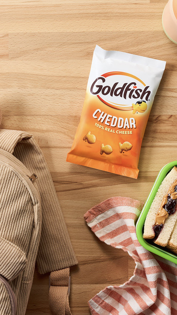 Goldfish Flavor Blasted Xtra Cheddar crackers with school supplies, a backpack, and a bowl of crackers.