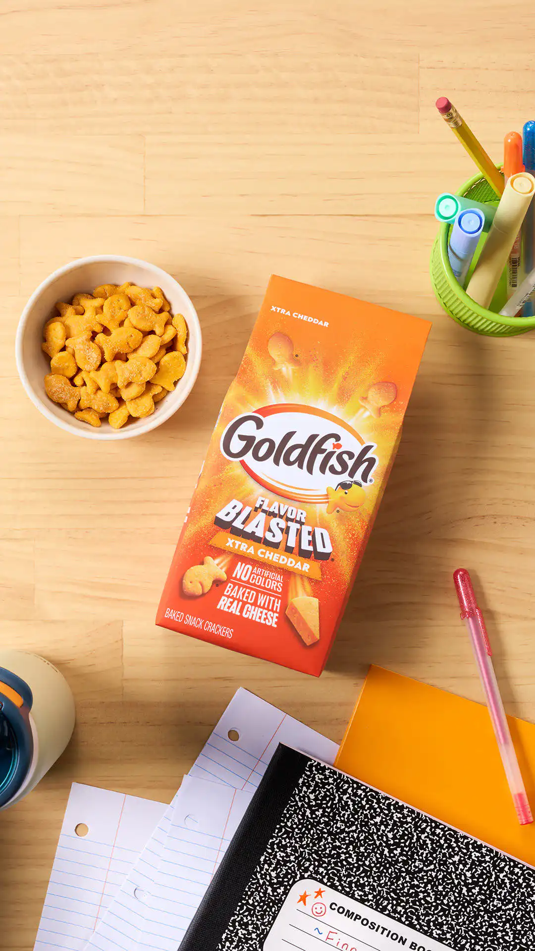 Goldfish Flavor Blasted Xtra Cheddar crackers with school supplies, a backpack, and a bowl of crackers.